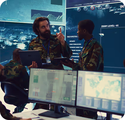 Two military personnel in camouflage uniforms discussing data with digital maps and screens in a command center.